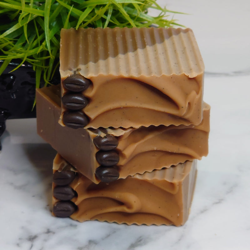 An exfoliating soap bar with the uplifting scent of coffee mixed with the sweet scent of vanilla. Coffee grinds are used for exfoliation in one half of the soap bar, the other half hydrates and moisturizes with soy milk and shea butter.
